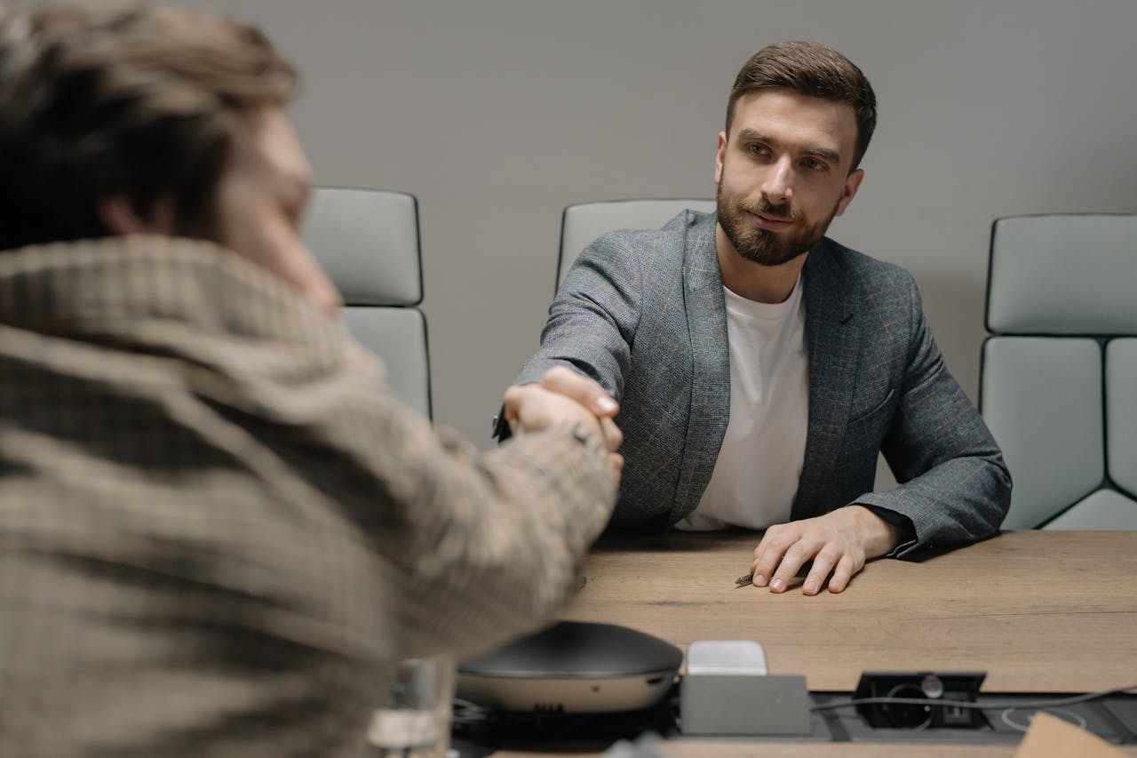 The Art of Drawing Readers In: Your attractive post title goes here Two businessmen shaking hands across a wooden desk in a modern office setting.